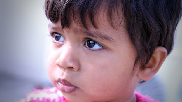Close-up portrait of a young South Asian child with expressive eyes outdoors in natural light.